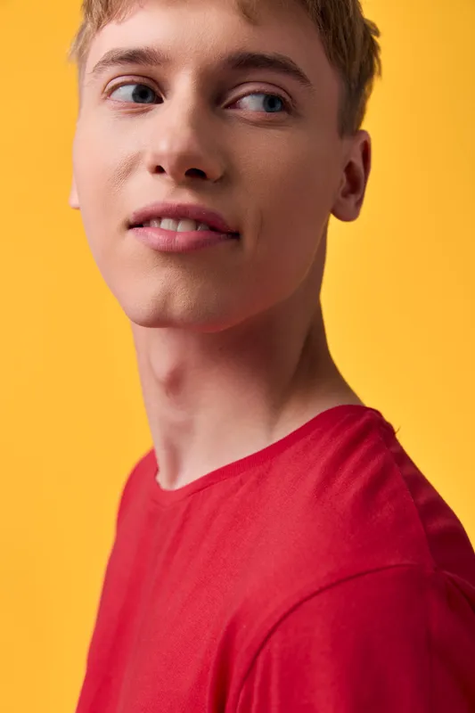 Close up of a young man in a red shirt against a bright yellow background, showcasing casual fashion, clear skin, confident expression, studio lighting and modern look.