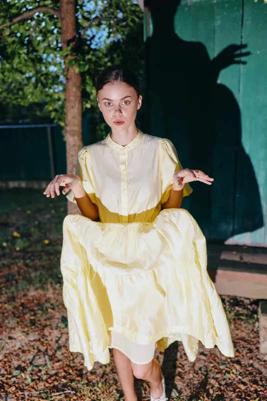 Woman in yellow vintage dress portrait at night with dramatic shadow and eerie hands on wall authenticity inclusivity in model expression and outdoor fashion