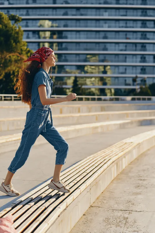 Lifestyle woman in modern boho-western denim street style walking outdoors, casual outfit with bandana and sneakers, film color effect, sunny urban background.
