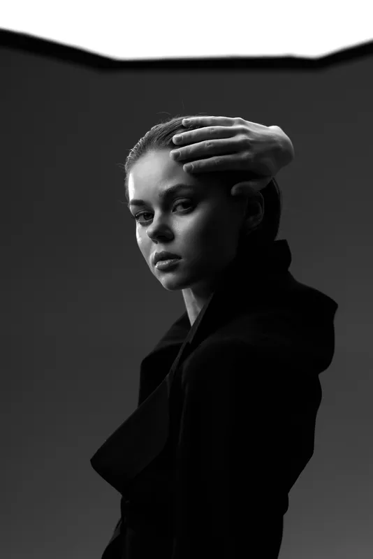 Black and white portrait of a thoughtful woman in dark coat with hand on forehead in moody lighting