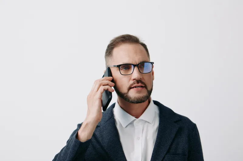 A professional man in business attire speaks on a cell phone against an isolated colored background, exuding confidence and focus during a crucial corporate moment.