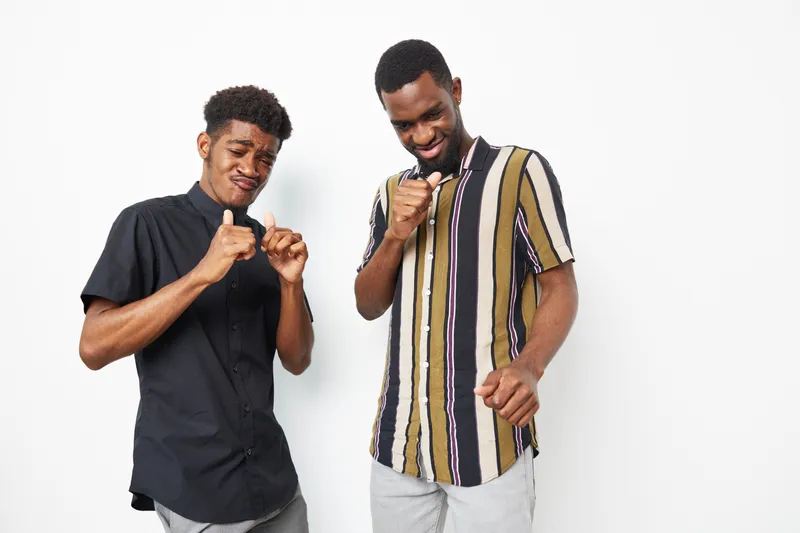Two smiling African American men enjoying music together, displaying happiness and connection. Their stylish outfits and cheerful expressions enhance the positive vibe.