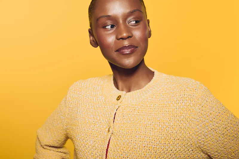 Confident African woman with dark skin wearing a yellow sweater poses against a bright yellow background. Concept of self-assurance, fashion, and vibrant color contrast in portrait photography.