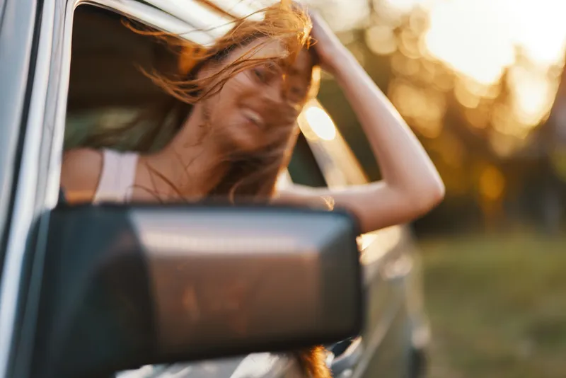 Young woman enjoying a road trip with her hair flowing in the wind, captured during a golden sunset, evoking feelings of freedom and adventure.