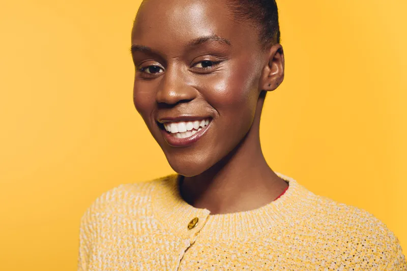 Smiling dark skinned African woman with clear skin wearing yellow sweater on yellow background. Portrait of happy black female model with natural beauty and confident expression.