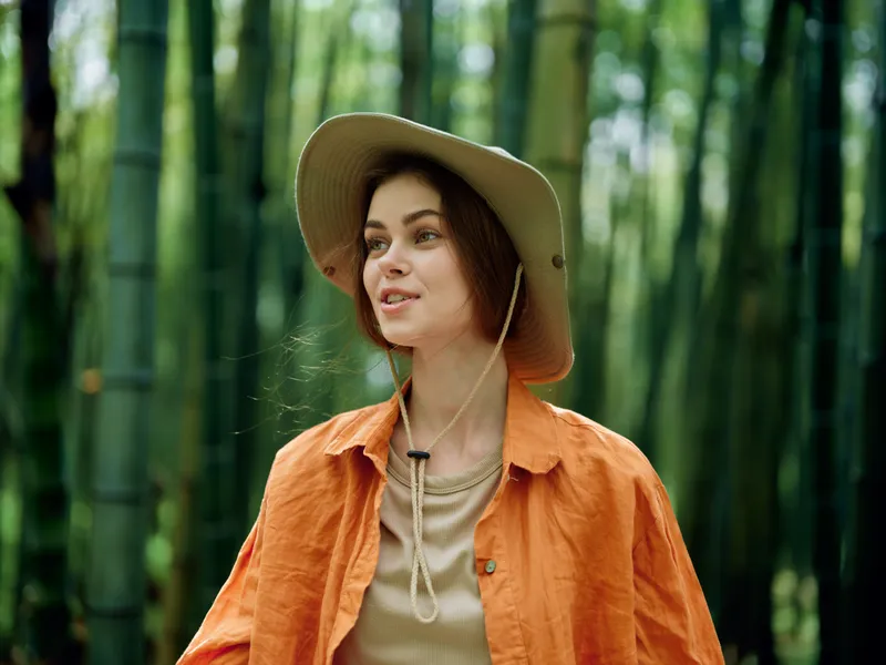 Woman bamboo hat forest nature portrait outdoors traveler in bamboo grove, young female wearing wide brim hat and orange shirt, smiling and exploring green serene woodland.