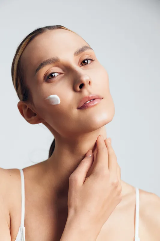 Woman skincare beauty portrait face cream on cheek neck treatment studio white background with hand at neck calm expression soft light smooth skin texture close up