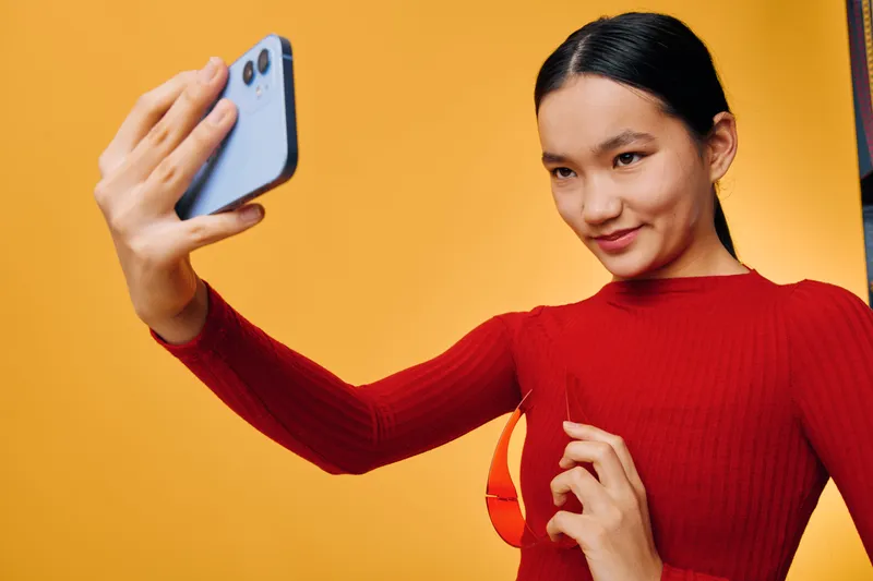 Woman, selfie, smartphone, and orange background with long sleeve sweater for social media content creation. Happy, portrait, young female holding phone for digital communication and selfie photo at