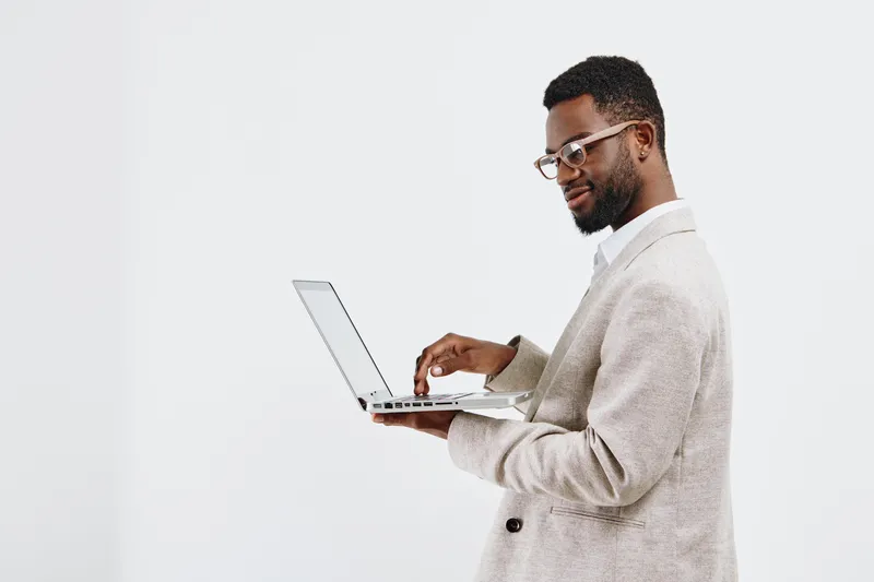 Confident smiling man with glasses using laptop computer in studio, wearing beige blazer, casual style, modern technology, white background, professional workspace, male professional.