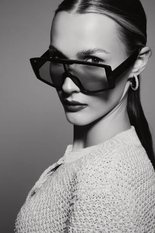 Stylish white woman with pale skin wearing large sunglasses and hoop earrings looks confident in black and white studio portrait.