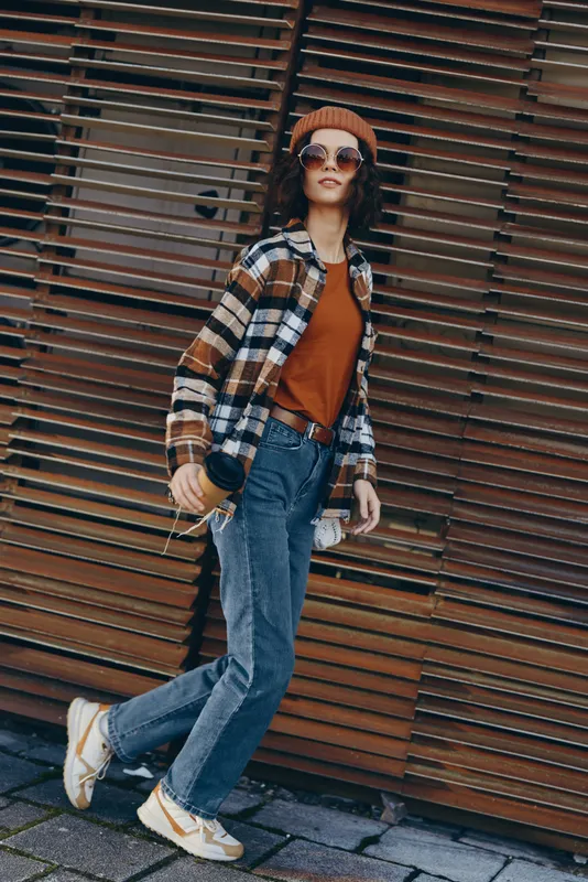 woman fashion street casual jeans sunglasses beanie coffee candid lifestyle authenticity golden hour glow: stylish urban portrait of a young woman walking with coffee and bottle, emotional