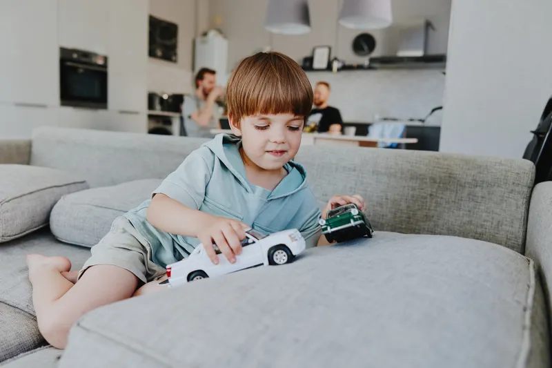 Happy boy playing with toy cars in a modern living room. The cheerful atmosphere is highlighted by cozy furniture and a bright interior, perfect for family moments.