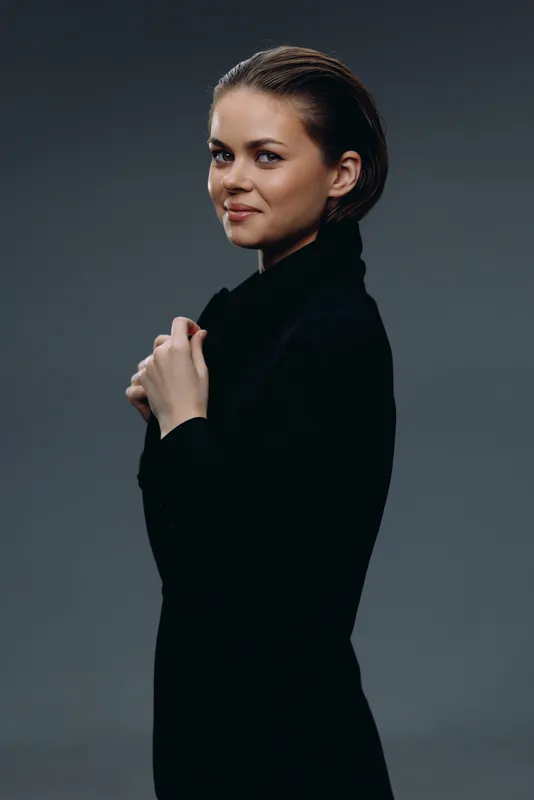 Smiling woman in black sweater with confident expression, dark background, portrait, casual style