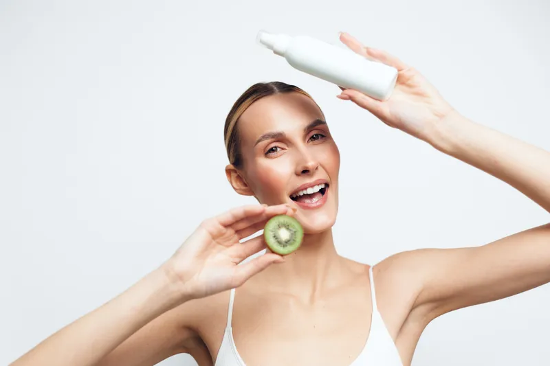 Woman uses skincare face toner with cucumber during beauty spa wellness self care on bright white studio background showing skin hydration glow and freshness