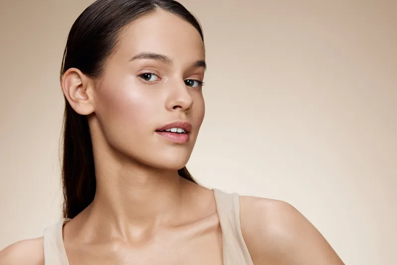 Natural beauty portrait of a young woman with flawless skin, showcasing a soft expression against a neutral background, ideal for wellness and skincare concepts