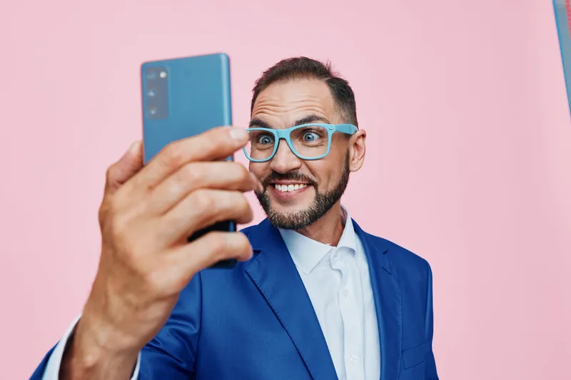 A professional businessman takes a vibrant self portrait against a solid pink backdrop, projecting confidence, enthusiasm, and focus in a clean, isolated setting.