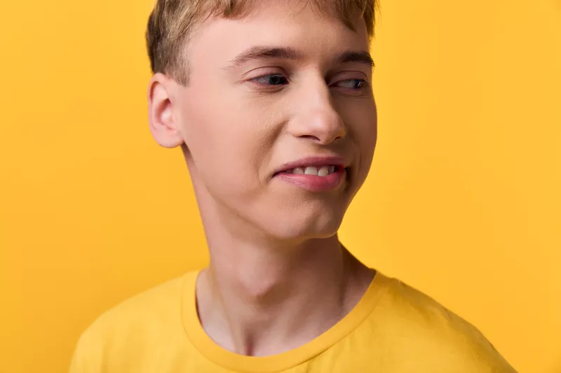 Sour expression on a teenage male wearing a yellow shirt against a bright yellow backdrop, capturing a candid moment of discomfort or hesitation with a playful mood.