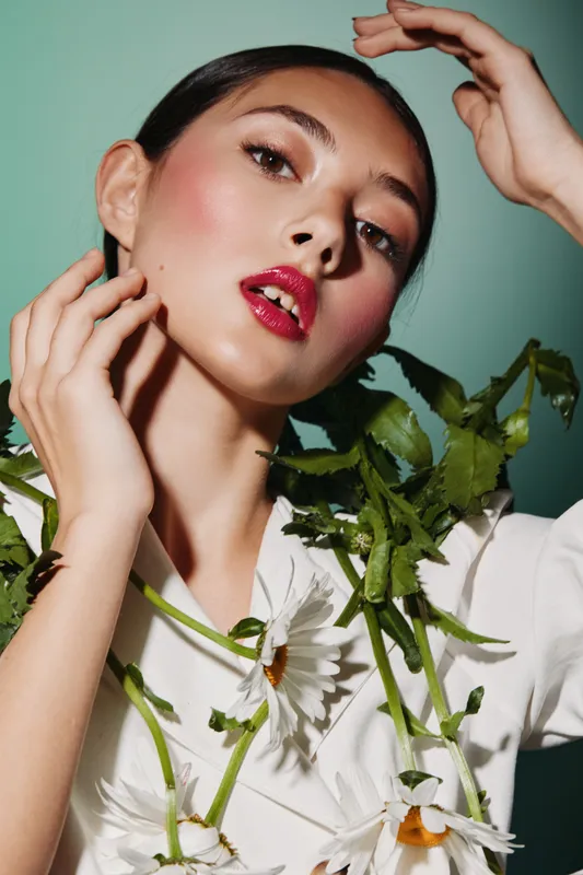 Elegant woman with glossy red lips and soft blush posing with white chamomile flowers on light green background. Beauty creative fashion concept mood portrait photo.