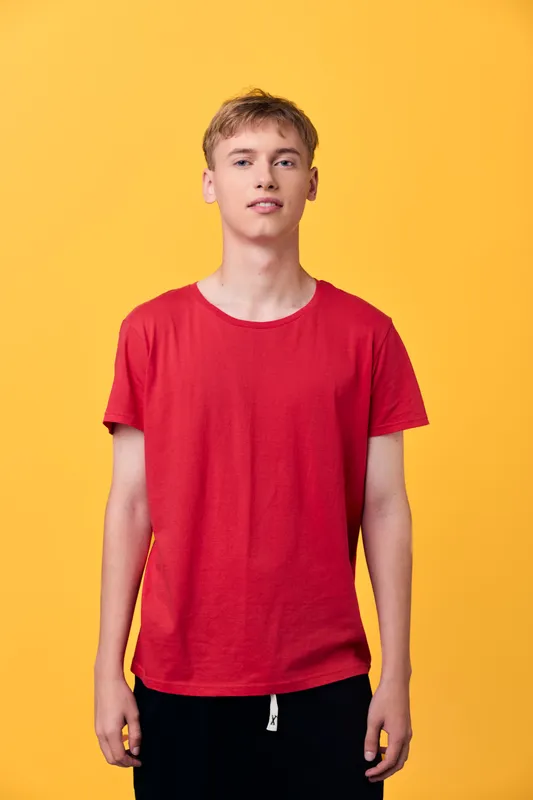 Young man wearing a red t shirt stands against a vibrant yellow backdrop, casual fashion styling with a clean studio shot, emphasizing color contrast and relaxed pose.