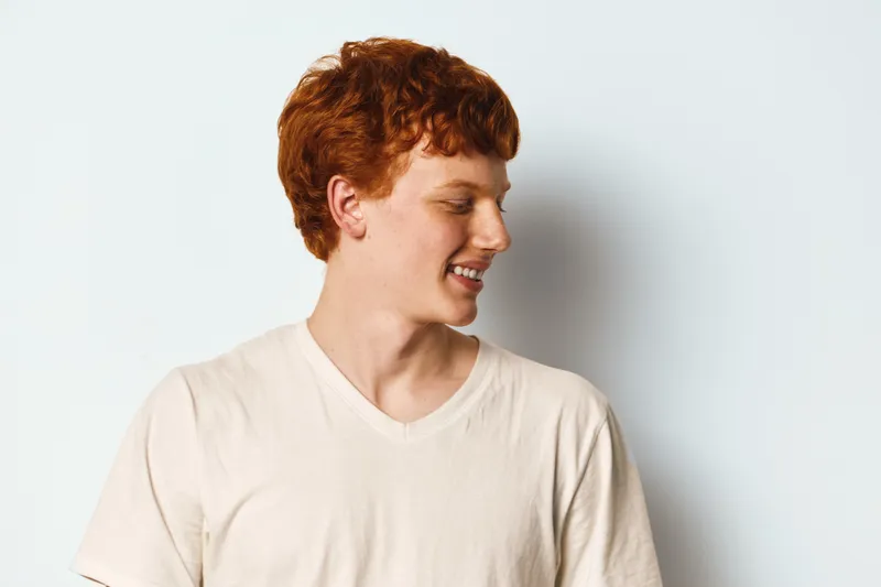 Young redhead man in beige t shirt smiling and looking aside on white background. Casual hairstyle, portrait with natural light and happy facial expression for lifestyle concept.