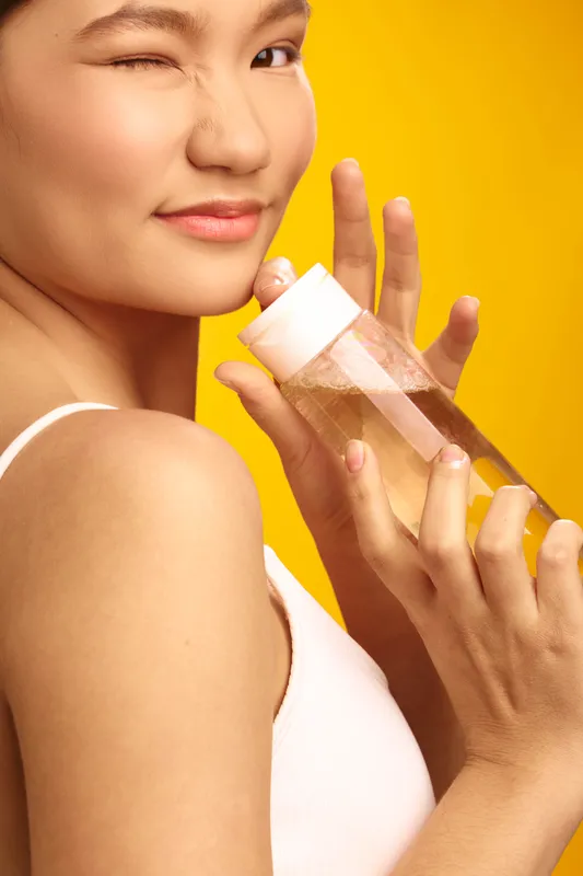 asian woman smiling while drinking from a water bottle in a bright studio setting. She holds the bottle with confidence, showcasing wellness and refreshment in a clean, vibrant composition.