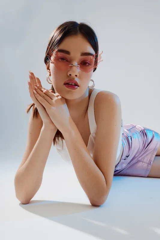 Young woman beauty fashion model wearing pink sunglasses and metallic skirt poses lying down on white background. Concept for style, elegance, and modern trends.