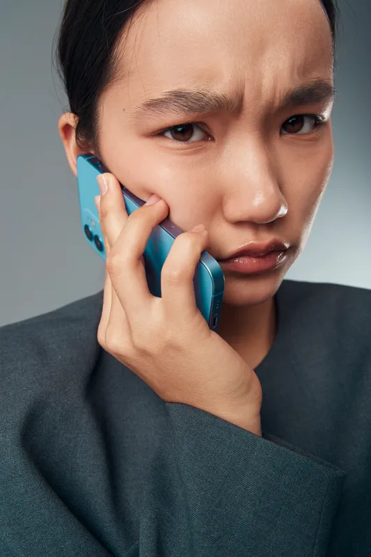Young woman with serious expression talking on smartphone close up, holding blue mobile device to ear, communicating or listening carefully with focused look and wrinkled forehead.
