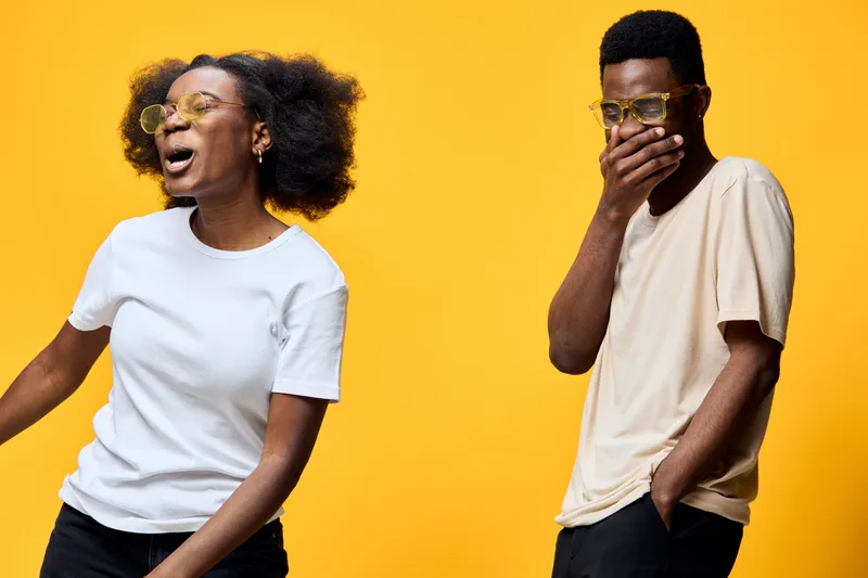 Joyful young African American couple laughing together against a bright yellow background wearing stylish glasses, conveying happiness and connection