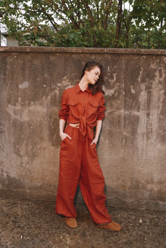 Woman lifestyle portrait of a woman in rust jumpsuit standing outdoors by a worn wall, casual pose, confident elegance, natural light, everyday fashion mood