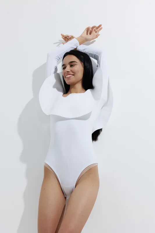 woman sport fitness in white athletic wear stretching arms upwards with relaxed expression against plain white background, fitness lifestyle concept