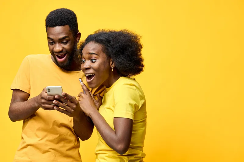Happy young couple engaging with smartphone, wearing matching yellow clothing, against a vibrant yellow background, showcasing joy and excitement with an inviting atmosphere