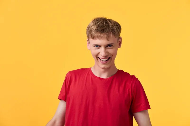 Smiling man in a red shirt against a yellow background in a studio shot, showcasing casual style, energetic mood and friendly confidence for lifestyle and fashion topics