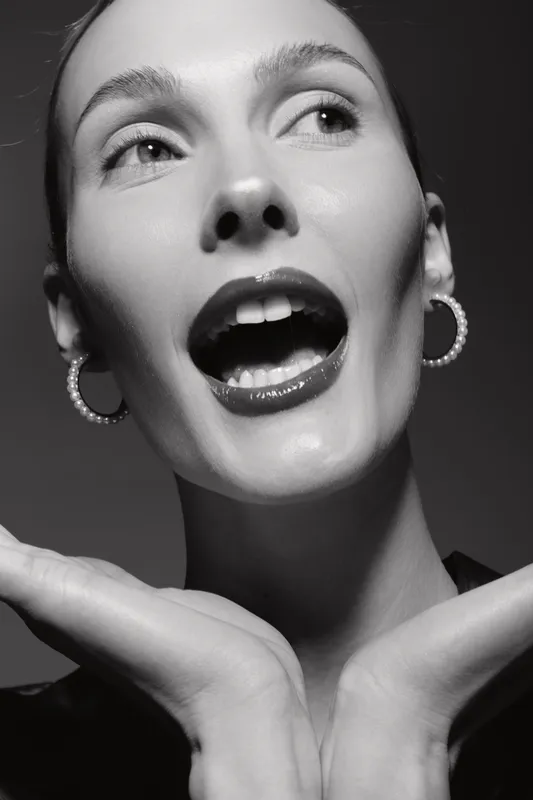 Closeup of white woman with pale skin and glossy lips, expressive face and pearl earrings. Studio portrait in black and white with dramatic lighting and emotion.