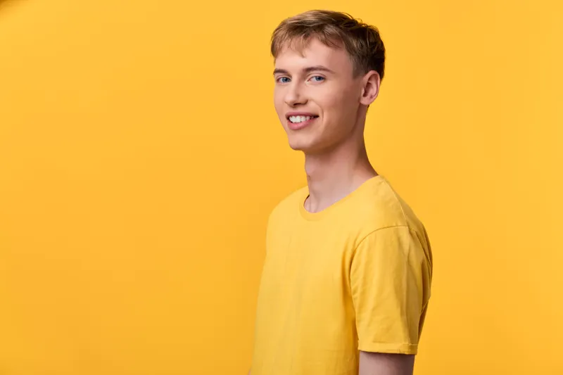 Smiling man in a bright yellow shirt stands against a vibrant yellow backdrop, conveying warmth, confidence, and casual style for fashion, lifestyle, or cheerful branding visuals