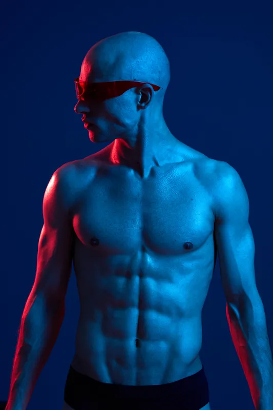 Muscular man in a dramatic blue and red lighting, showcasing strength and fitness. The striking color contrast emphasizes the subject's intensity and determination.