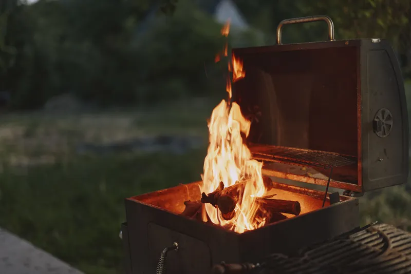 Cozy outdoor barbecue with a grill full of flames, set in a green garden, highlighting summer vibes and the joy of outdoor cooking