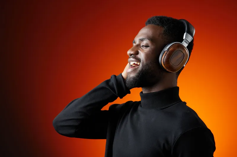 Happy young man enjoying music with headphones in a stylish black turtleneck on a warm orange background, showcasing joy and relaxation