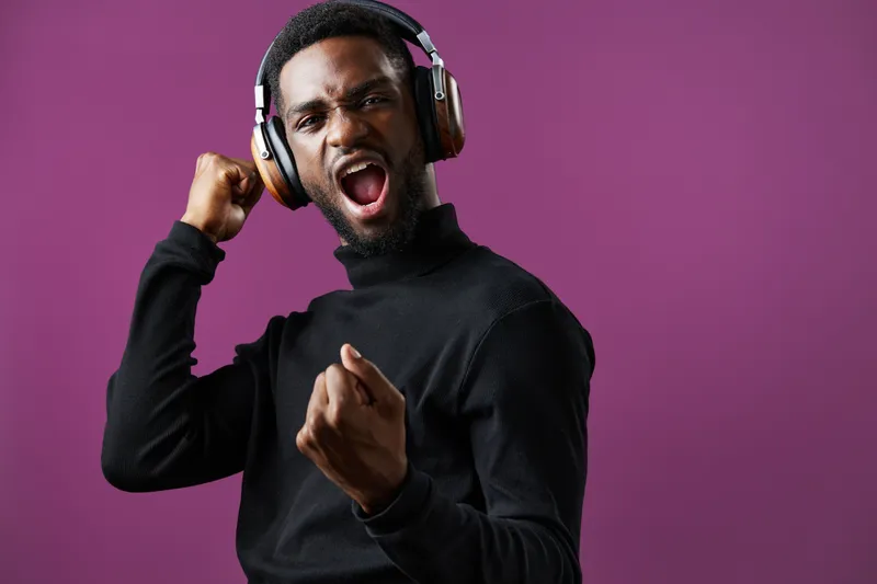Young Black man celebrating with headphones on a purple background, expressing joy and excitement through music and dance