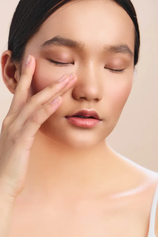 asian woman rests her face softly, eyes closed, and fingers touch her cheek in a serene skincare moment, creating a calm, gentle mood and a sense of quiet self care.