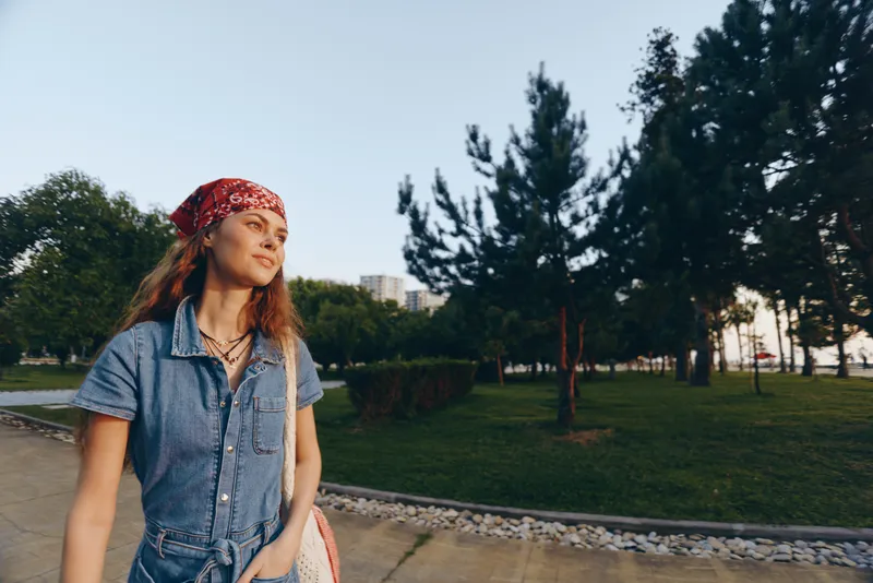 lifestyle woman in modern boho-western denim street style wearing red bandana outdoors with natural trees film color warm tones