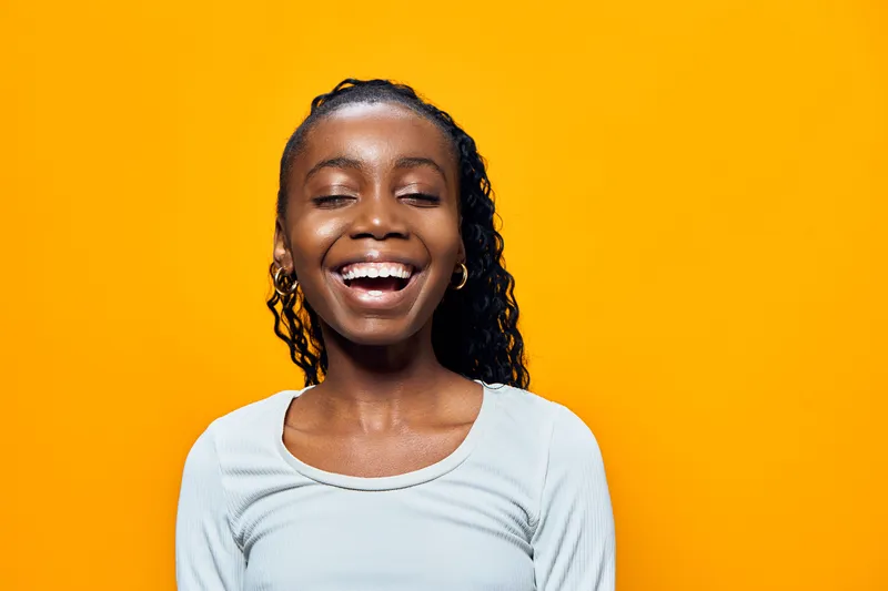 A joyful young girl with curly hair smiling against a vibrant yellow background, showcasing happiness and positivity, perfect for children s content