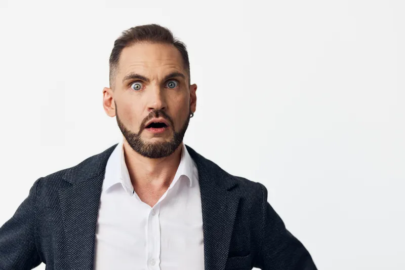 A professional businessman with a surprised expression stands against an isolated colored background, conveying strong emotion, focus, and confidence in a modern corporate setting.