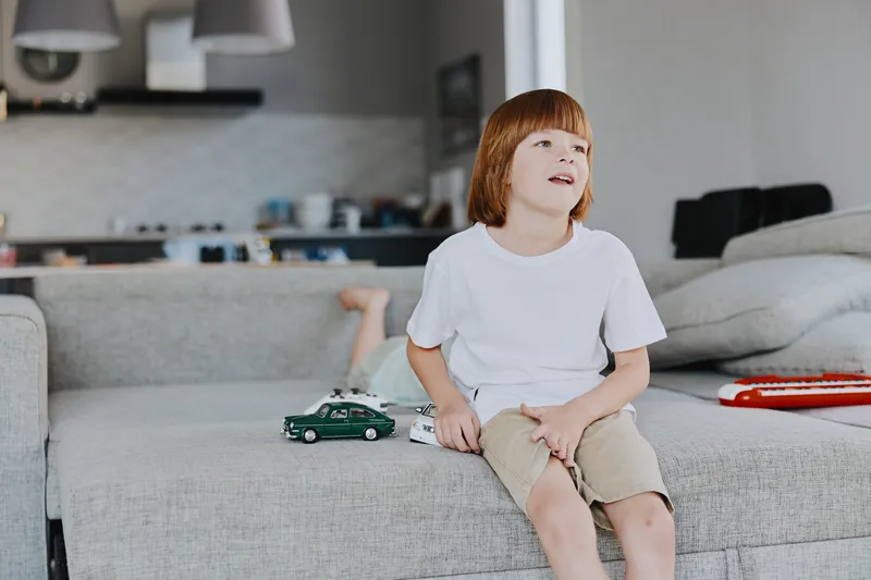 Happy boy playing with toy cars in a cozy living room, showcasing a playful atmosphere and warm interior decor for family-oriented content.