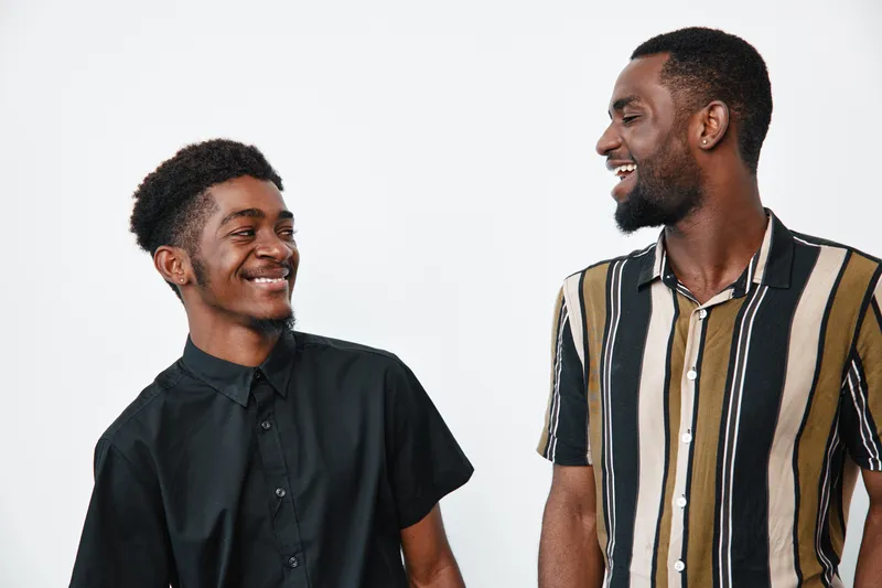 Two african american men smiling and looking at each other in casual clothes with dark skin and short hair on white background for friendship and happiness.