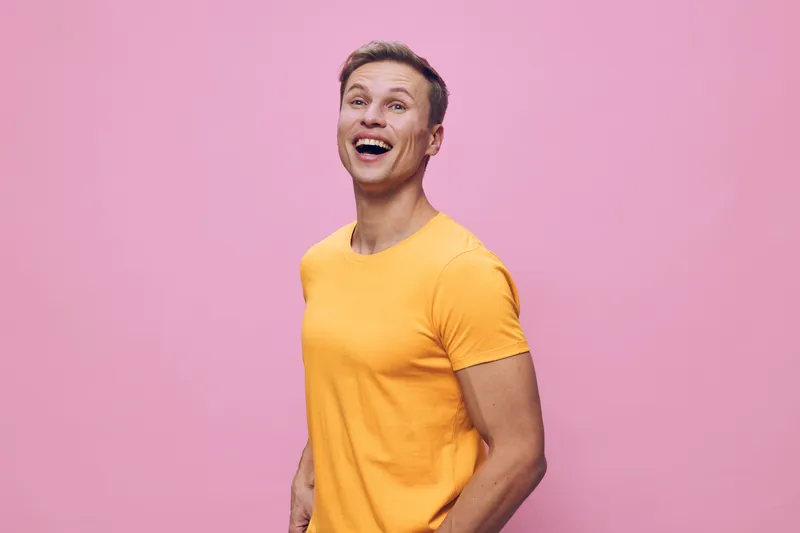 Smiling young man wearing bright yellow t-shirt looking happy and cheerful stand against pink background studio portrait portrait. People lifestyle concept
