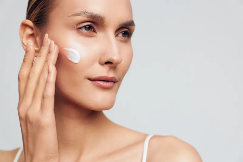 Young woman applies moisturizing cream on her face with fingers close up portrait natural skincare routine healthy skin isolated on white background beauty concept.