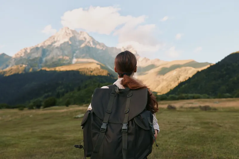 Woman with backpack hiking in mountain landscape during daytime. Outdoor adventure, nature exploration, and active lifestyle concept. Clear sky and sunlight create peaceful mood.