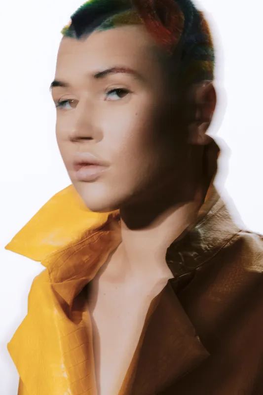 Woman with blurred motion effect wearing a yellow leather jacket, featuring soft lighting and a smooth neutral background for a modern artistic portrait.