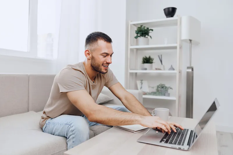 Smiling man engaged in remote work in a cozy home environment, showcasing productivity and comfort with a modern design and soft color palette.
