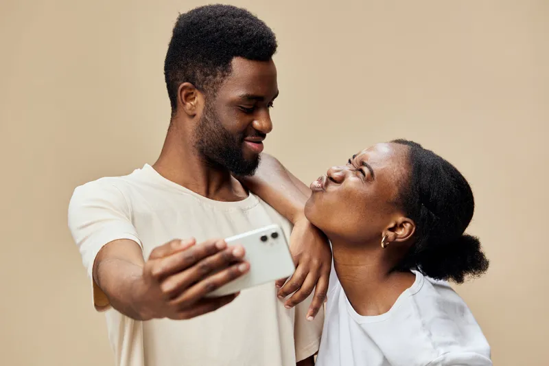 Happy young African couple taking a selfie together, showcasing love and joy in a light background setting, perfect for social media content